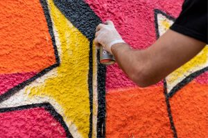 En hand som håller i en sprayburk och som målar en färgglad vägg i grafitti/street art. En av flera TIA-aktiviteter som erbjuder unga asylsökande och flyktingar möjlighet att skapa streetart hos StudioUng.